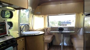 A compact RV kitchen with a stove, sink, and a small dining table. - It's Another Beautiful Day At Whidbey Rose in Langley, On Whidbey Island (Langley)