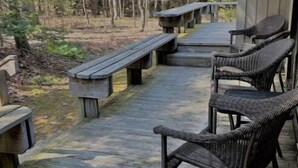 A wooden deck with benches and wicker chairs, surrounded by trees. - Beach/Ski Home in Harbor Springs (Harbor Springs)