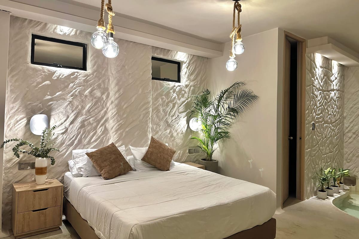 A modern bedroom with a large bed, bedside tables, a mirror, and a wall-mounted light fixture.