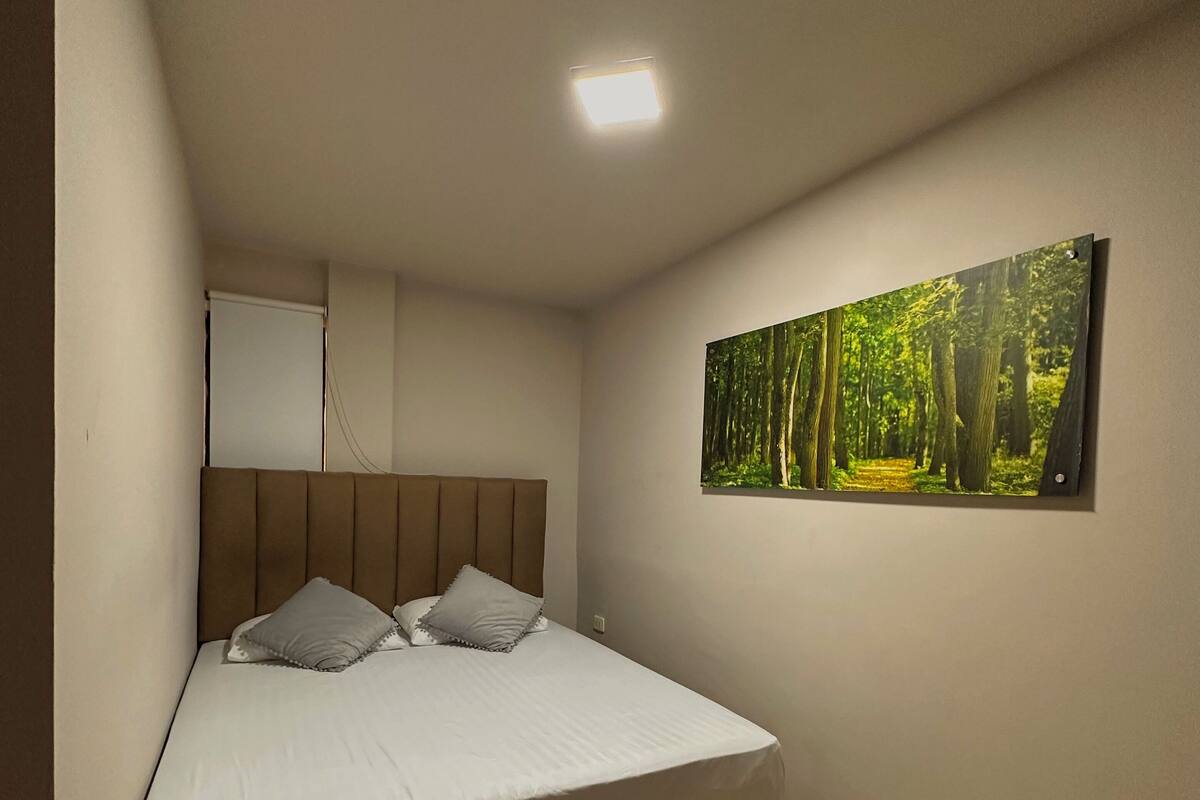 A bedroom with a bed, a headboard, a wall-mounted picture, and a ceiling light.
