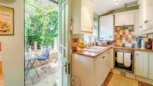 Una cocina con armarios blancos, salpicadero de azulejos y ventana con vista a un jardín.