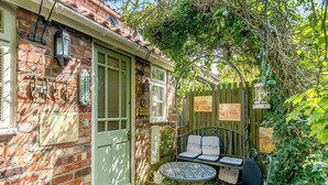 Una casa de ladrillo con una puerta verde, un pequeño patio con una mesa y sillas, y una valla de madera.
