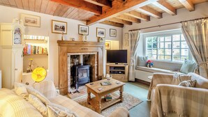 Un salón acogedor con chimenea, vigas de madera, televisión y asientos cómodos.