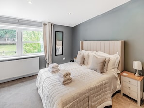 Een slaapkamer met een groot bed, nachtkastje, spiegel en een raam met gordijnen.