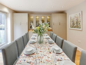Een eetkamer met een lange tafel gedekt voor zes personen, omringd door grijze gestoffeerde stoelen.