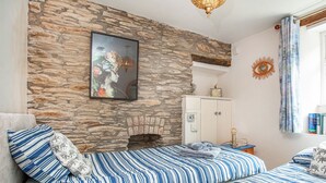 Una habitación con pared de piedra, chimenea, cama con ropa de cama a rayas, un armario y una ventana con cortinas.