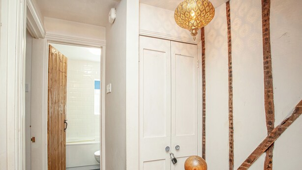 Un pasillo con puerta de madera, pared blanca con textura y un objeto decorativo de madera.