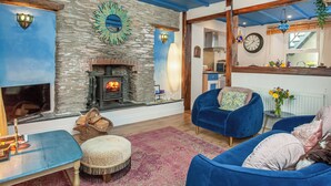 Una sala de estar acogedora con chimenea de piedra, muebles tapizados en azul y una cocina visible a través de un vano abierto.