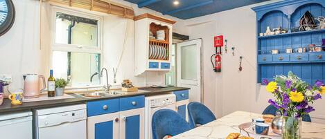 A kitchen with a dishwasher, sink, and blue cabinets. There is a dining table with chairs and a vase of flowers.