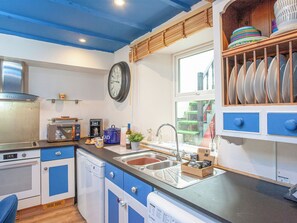 A kitchen with a clock, a coffee machine, and a window with a view of a staircase. - 2 bedroom accommodation in Polruan, near Fowey (Polruan, near Fowey)