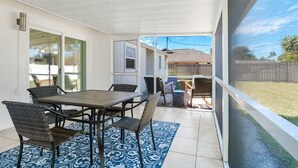 A covered patio with a table and chairs, a blue patterned rug, and a view of a backyard.
