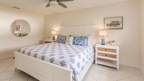 A bedroom with a bed, a round mirror, two bedside tables with lamps, a ceiling fan, and a framed picture on the wall.