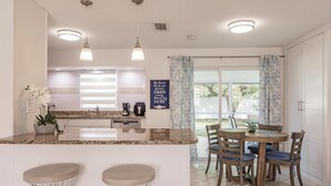 A modern kitchen with a central island, bar stools, and a dining area with wooden chairs.