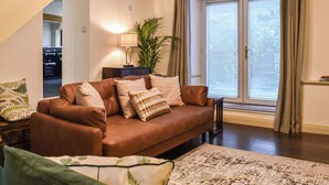 A living room with a brown sofa, patterned cushions, a patterned rug, a lamp, and a large window with curtains. - 2 bedroom accommodation in Ambleside (Ambleside)