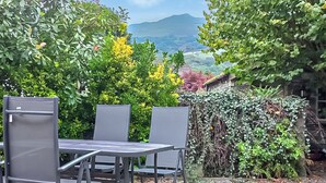 An outdoor patio with a table and four chairs, surrounded by lush greenery and a view of distant hills. - 2 bedroom accommodation in Ambleside (Ambleside)