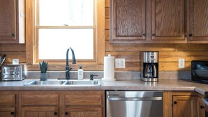 A kitchen with wooden cabinets, a stainless steel dishwasher, a coffee maker, a toaster, and a window above the sink.