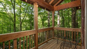 A wooden deck with metal chairs and a railing, surrounded by a forest.
