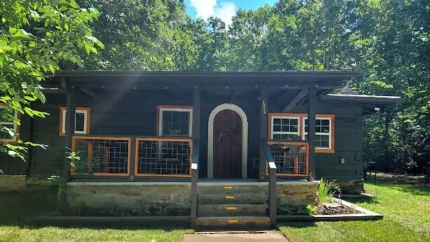 Una casa pequeña de una sola planta con un porche delantero, una puerta de madera y un jardín.