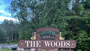 A wooden sign with "The Woods" and "Jill Brook" written on it, surrounded by grass and trees. - Spacious White Mt. Cabin - Outdoor Patio & Fireplace (Thornton)