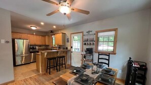 A modern kitchen with wooden cabinets, a stainless steel refrigerator, and a dining area with a table set for four. - Spacious White Mt. Cabin - Outdoor Patio & Fireplace (Thornton)