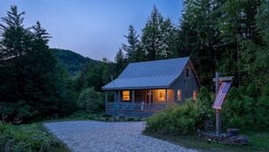 A rustic cabin with a stone pathway leading to the entrance, surrounded by dense forest. - Spacious White Mt. Cabin - Outdoor Patio & Fireplace (Thornton)