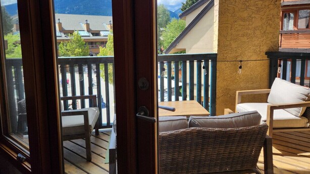 A balcony with wicker furniture, a wooden table, and a view of mountains. - The Ikon | Lofted Studio with King Bed + Patio (Whistler)