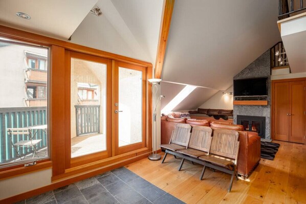 Un acogedor dormitorio tipo loft con un amplio ventanal corredera que da a un balcón, una chimenea y techo de madera.