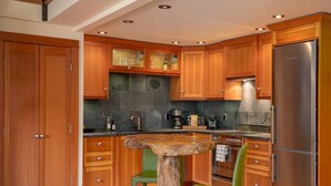 A kitchen with wooden cabinets, a stainless steel refrigerator, a wooden table, and a green chair. - The Ikon | Lofted Studio with King Bed + Patio (Whistler)