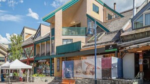 A multi-story building with a green balcony, a sign for 'New Leaf', and a 'Coming Soon' banner. - The Ikon | Lofted Studio with King Bed + Patio (Whistler)