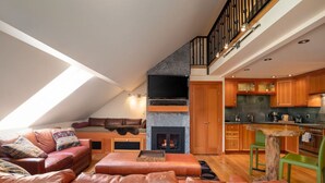 A loft-style living area with a fireplace, leather sofas, a dining table, and a kitchen with wooden cabinets. - The Ikon | Lofted Studio with King Bed + Patio (Whistler)