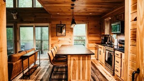 A wooden cabin interior with a dining area, kitchen, and large windows.