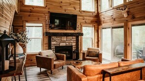 A cozy cabin interior with a fireplace, wooden walls, and a television.