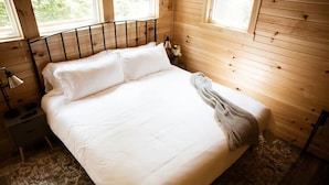 Un lit bien fait, avec du linge de lit blanc, dans une chambre d’une cabane en bois.