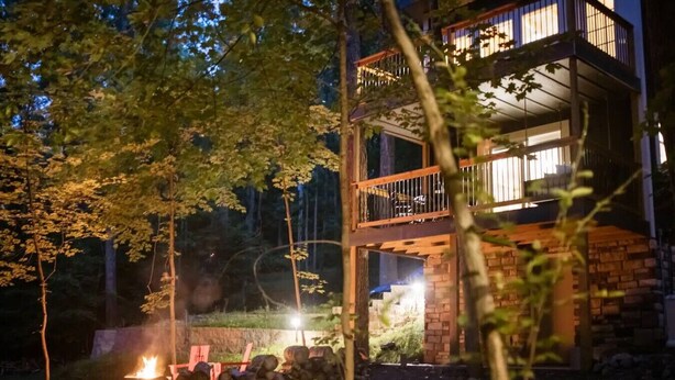 Un bâtiment à deux étages doté d’un balcon, entouré d’arbres et éclairé par un feu de joie.