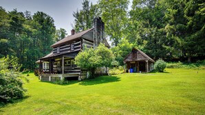 Eine Blockhütte mit Veranda und einem Nebengebäude in bewaldeter Landschaft.