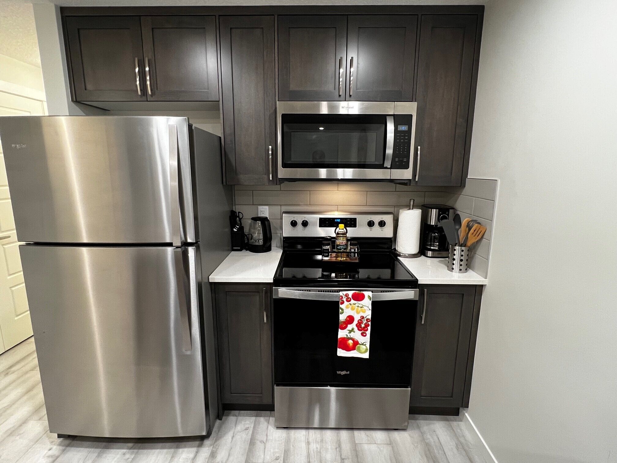 A modern kitchen with stainless steel appliances, dark cabinets, and a white countertop.