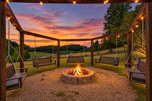 A wooden pergola with a fire pit in the center, surrounded by swings and a gravel ground. - Sleeps 16 | Hot Tub + Game Room + Trails (Sarahsville)