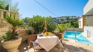 Un patio con una mesa preparada para dos, con vista a una piscina y edificios a lo lejos.