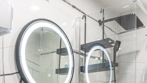 A modern bathroom with a round mirror, a white sink, and a glass-enclosed shower area. - Apartment & Rooms Primi - Studio with Balcony (Dubrovnik)