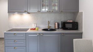 A kitchen with grey cabinets, a black countertop, a sink, a kettle, a microwave, and a chair. - Apartment & Rooms Primi - Studio with Balcony (Dubrovnik)