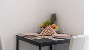 A dining table set with pink plates, gold cutlery, and a fruit bowl containing bananas, grapes, apples, and a pineapple. - Apartment & Rooms Primi - Studio with Balcony (Dubrovnik)