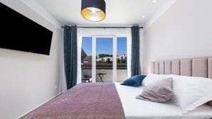 A modern bedroom with a large bed, a flat-screen TV, and a balcony with a city view. - Apartment & Rooms Primi - Studio with Balcony (Dubrovnik)
