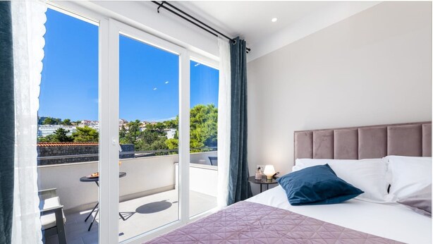 A bedroom with a large bed, a nightstand, and a view of a balcony with outdoor furniture. - Apartment & Rooms Primi - Studio with Balcony (Dubrovnik)