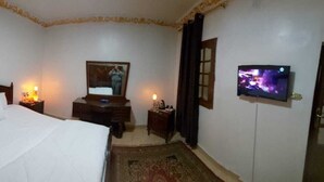 A hotel room with a bed, a dresser, a television, and a door. - TUI Pyramids View  (Giza)