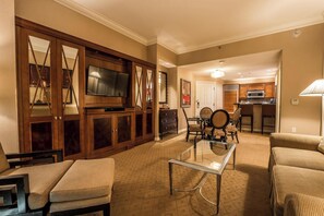 Relax in this stylish living room with a large flat-screen TV, comfortable seating, and a kitchen area.