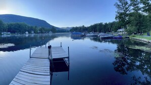 A calm lake with a wooden dock extending into the water, surrounded by trees and boats.