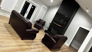 Un salon moderne doté d’un grand canapé d’angle, de deux fauteuils, d’une cheminée et d’un ventilateur de plafond.