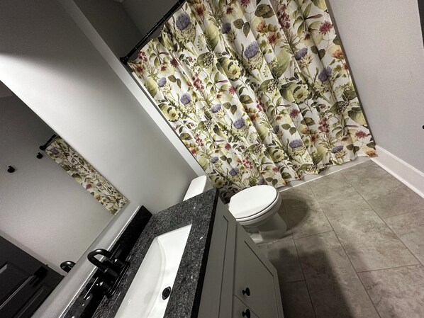 A bathroom with a white sink, a toilet, and a shower curtain with a floral pattern. - Modern 3 BR home, interior lot near Lake Keowee, Clemson, Walhalla, Seneca. (Seneca)