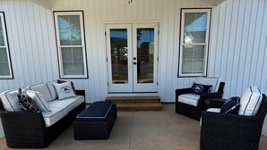 Une terrasse couverte avec deux canapés en osier et un banc, des murs blancs et une porte vitrée.