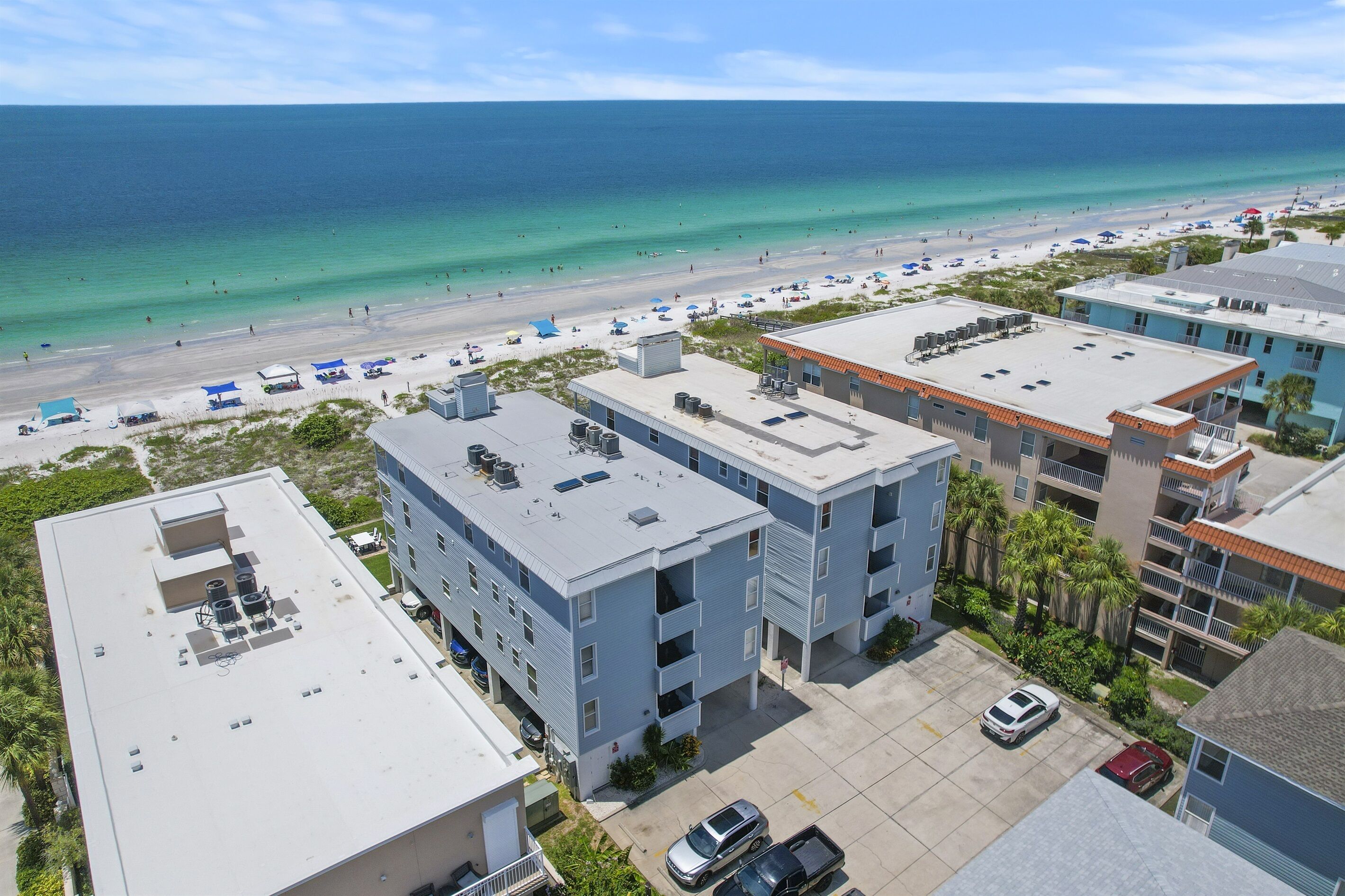 A beachfront hotel with multiple buildings, a parking lot, and a beach in the background.